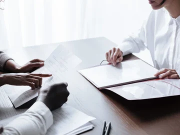 Three adults sit at a table reviewing papers and household documents during a calm meeting.