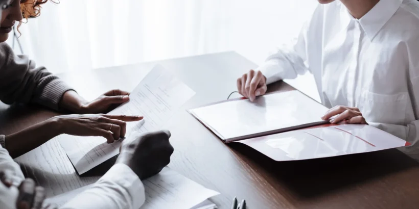 Three adults sit at a table reviewing papers and household documents during a calm meeting.