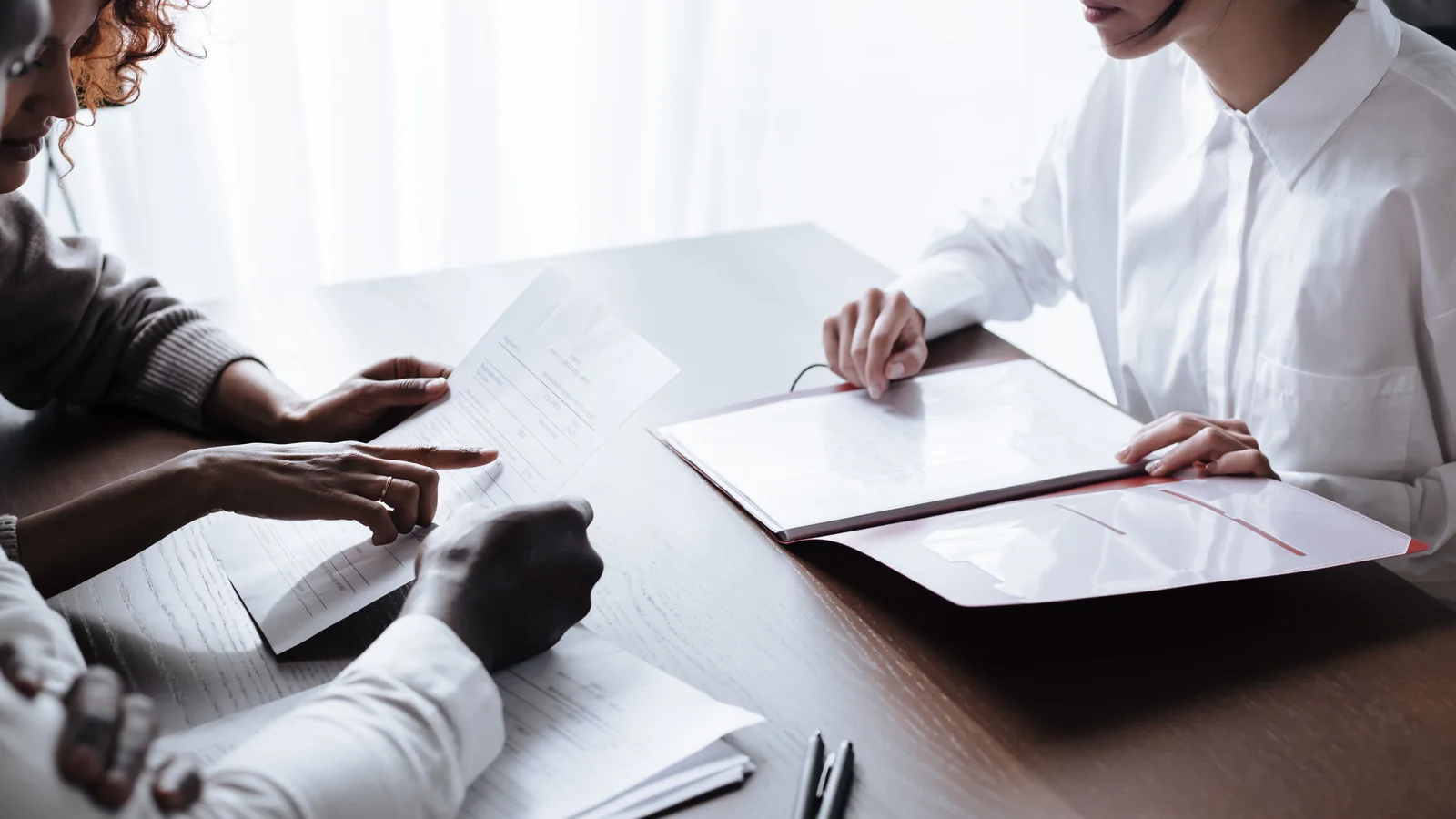Three adults sit at a table reviewing papers and household documents during a calm meeting.