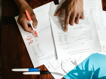 Overhead view of hands reviewing and highlighting documents spread across a wooden desk.