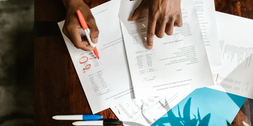 Overhead view of hands reviewing and highlighting documents spread across a wooden desk.
