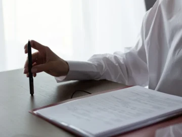 A professional in a white shirt reviews paperwork at a desk while holding a pen.