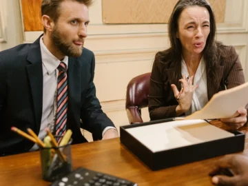 Two legal professionals discuss documents across a conference table in a professional office.