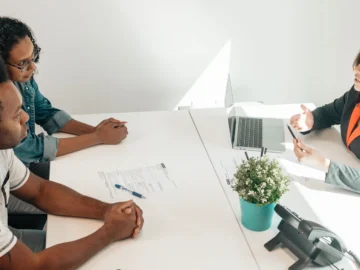 Two adults meet with a legal professional at a bright office table, reviewing paperwork together.