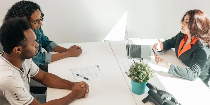 Two adults meet with a legal professional at a bright office table, reviewing paperwork together.