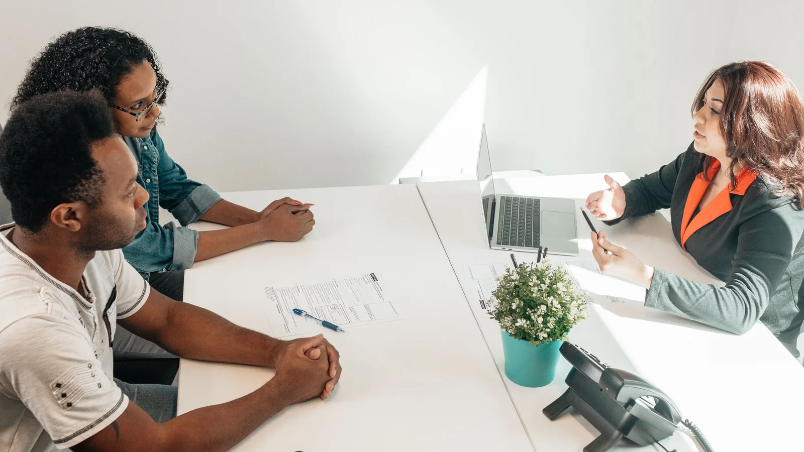 Two adults meet with a legal professional at a bright office table, reviewing paperwork together.