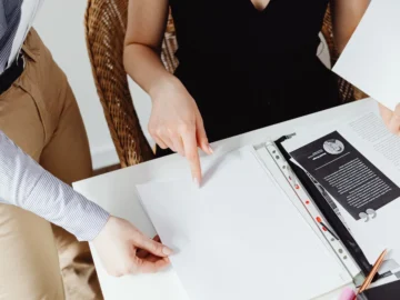 Two people review paperwork together at a table, with one person pointing to a document.