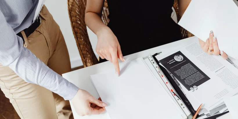 Two people review paperwork together at a table, with one person pointing to a document.