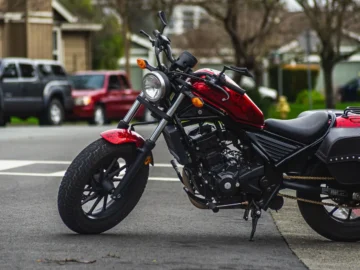 Red motorcycle parked on an urban street near a tree-lined intersection.