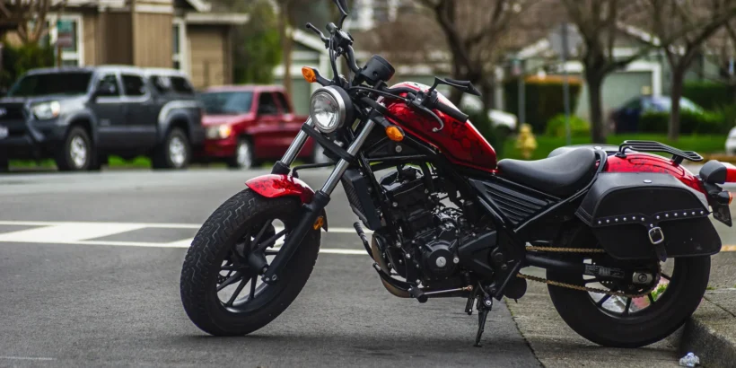 Red motorcycle parked on an urban street near a tree-lined intersection.