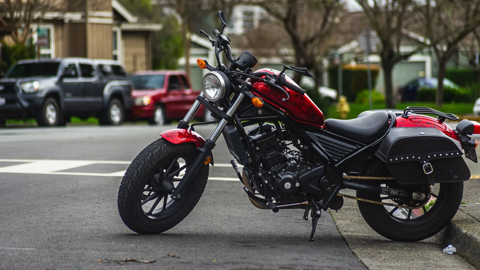 Red motorcycle parked on an urban street near a tree-lined intersection.