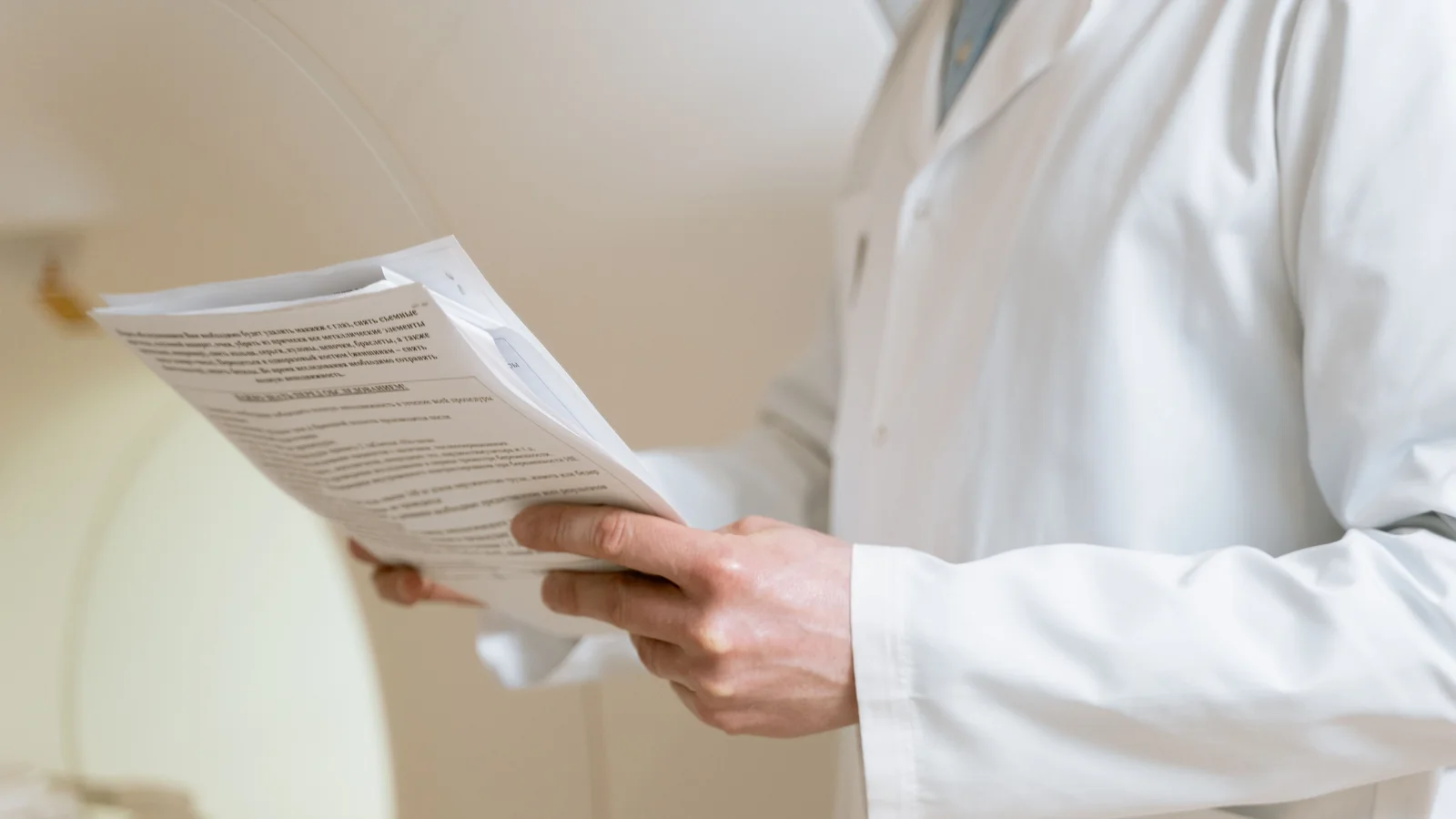 Healthcare professional in a white coat holding and reviewing paperwork in a softly lit clinical setting.