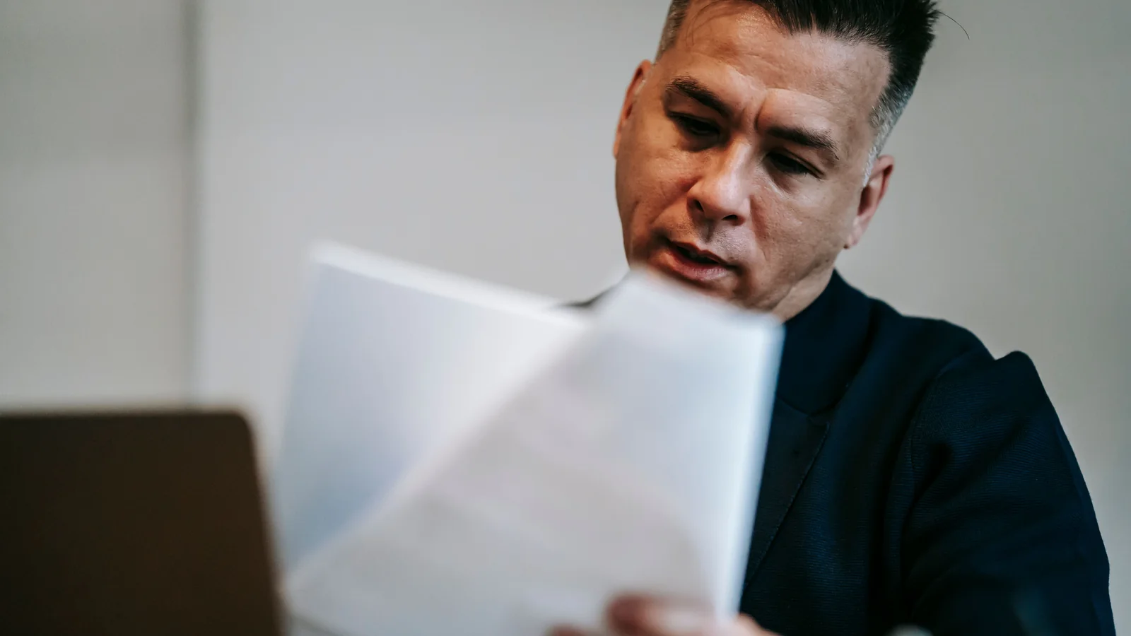A professional man reviews paperwork at a desk indoors.
