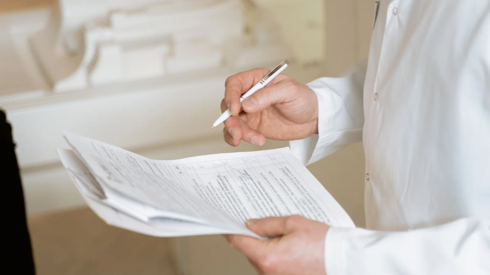 Close-up of a healthcare professional holding medical documents and writing notes in a bright clinical setting.