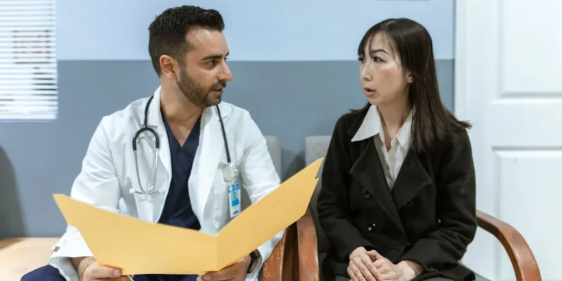 Doctor and patient seated in a clinic reviewing a yellow folder together.