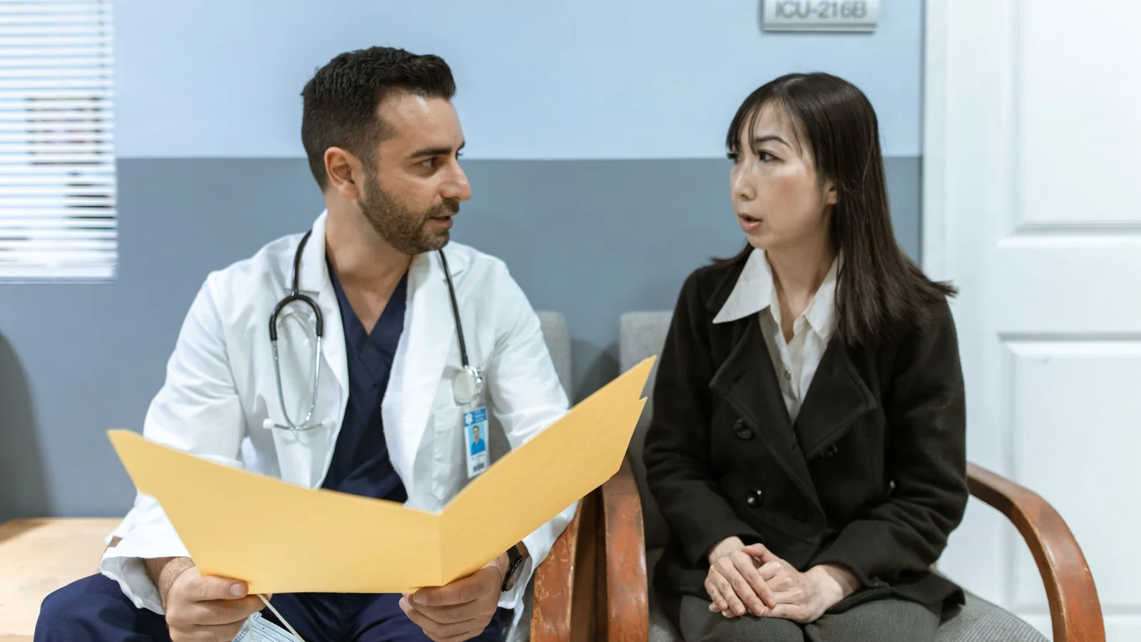 Doctor and patient seated in a clinic reviewing a yellow folder together.